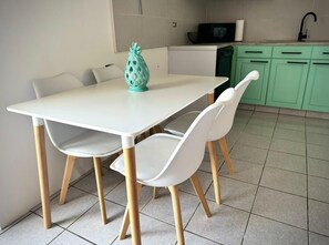 A small, modern kitchen with a white table and chairs, a green cabinet, and a microwave.