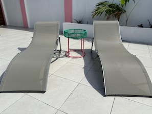 Two lounge chairs with a table and a green basket between them.