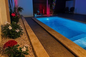A swimming pool with a tiled edge, surrounded by a pebble bed and flowering plants.