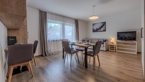 Een moderne woonkamer met een eethoek, houten vloeren, een televisie en een schilderij aan de muur.