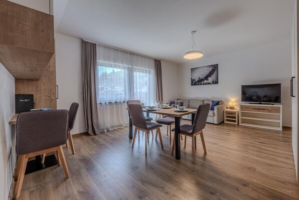 A modern living room with a dining area, wooden flooring, a TV, and a painting on the wall. - Holiday Apartment in Jochberg Near the ski Lift (Jochberg)