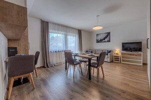 Ein modernes Wohnzimmer mit Essbereich, Holzboden, Fernseher und einem Gemälde an der Wand.