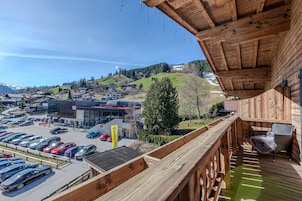 Eine Holzterrasse mit Korbmöbeln, die auf einen Parkplatz und ein Gebäude mit der Aufschrift 'ZACHAER' blickt.