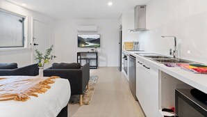 Een compacte hotelkamer met een bed, een zithoekje, een kitchenette en uitzicht op een landschap door het raam.