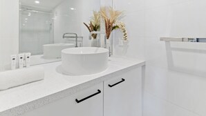 Een moderne badkamer met een wit wastafel, meubel en spiegel. Er staan decoratieve planten op het aanrecht en er ligt een handdoek op de wastafel.