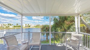 A covered outdoor area with white chairs and a view of a lake and buildings.