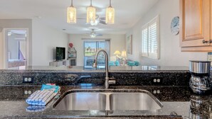 A kitchen with granite countertops, stainless steel sink, and pendant lighting.