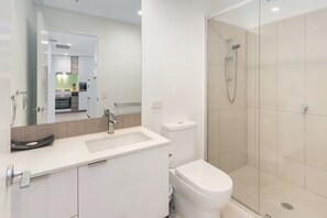A modern bathroom with a white sink, toilet, and glass-enclosed shower. - Beautiful Unit With Gym and Pool Near Museums (Brisbane)