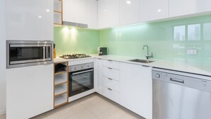 A modern kitchen with white cabinets, a stainless steel microwave, oven, and dishwasher, and a green backsplash. - Beautiful Unit With Gym and Pool Near Museums (Brisbane)