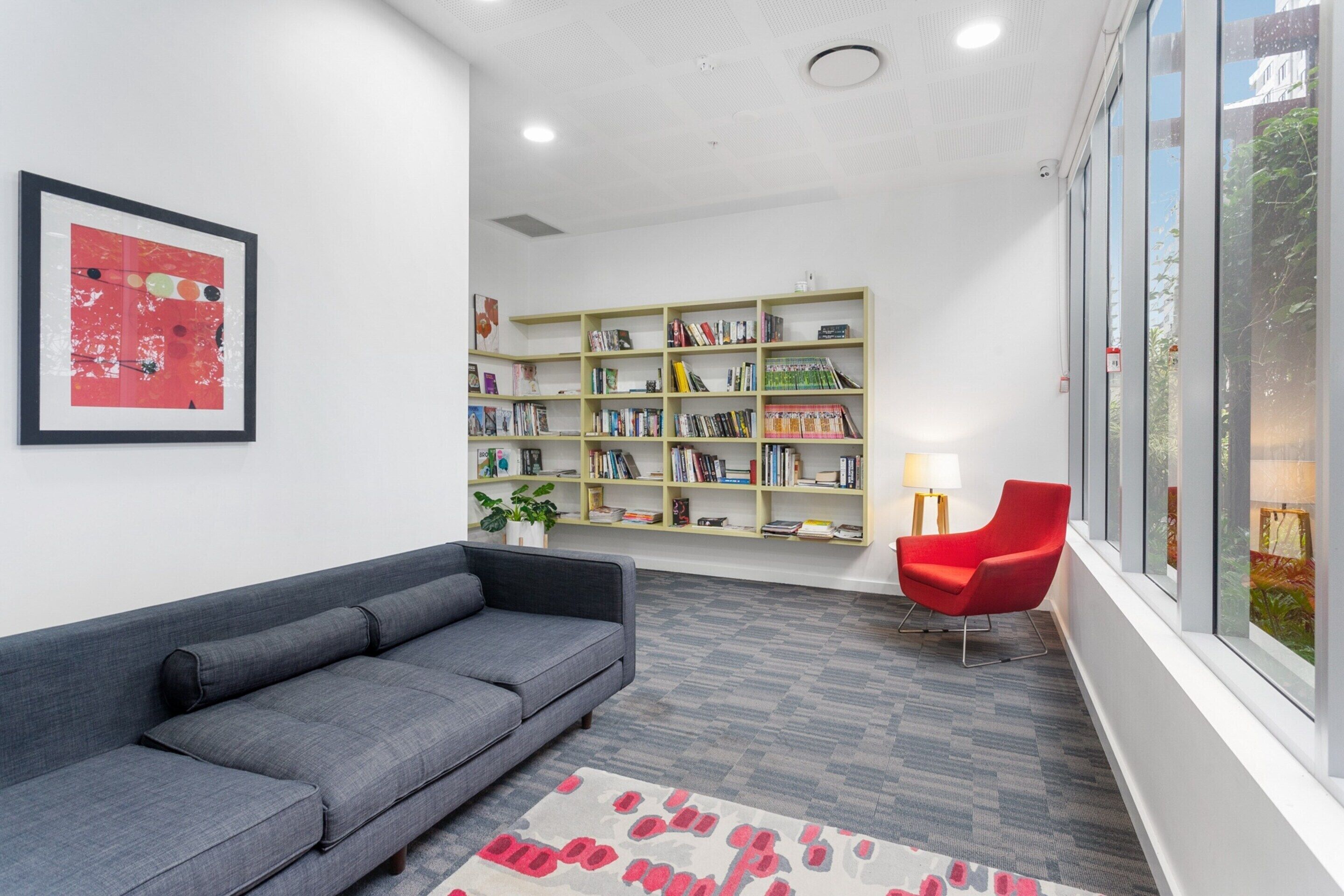 A modern library with a grey sofa, a red chair, and a bookshelf filled with books.