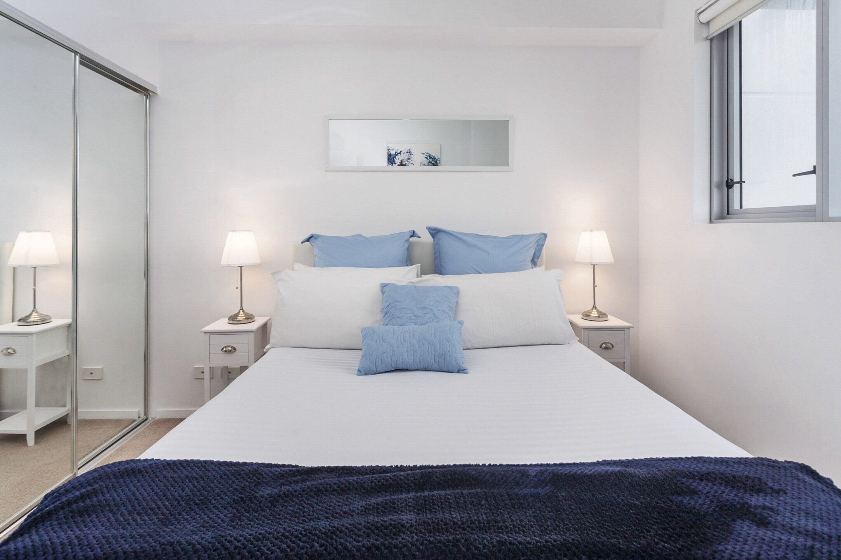 A bedroom with a bed, two bedside tables with lamps, a mirror, and a window.