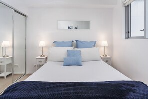 A bedroom with a bed, two bedside tables with lamps, a mirror, and a window. - Beautiful Unit With Gym and Pool Near Museums (Brisbane)