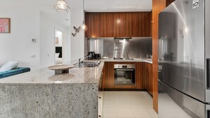 A modern kitchen with a central island, stainless steel appliances, wooden cabinets, and pendant lighting.