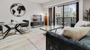 A modern living room with a glass dining table, black leather sofa, and a large world map artwork.