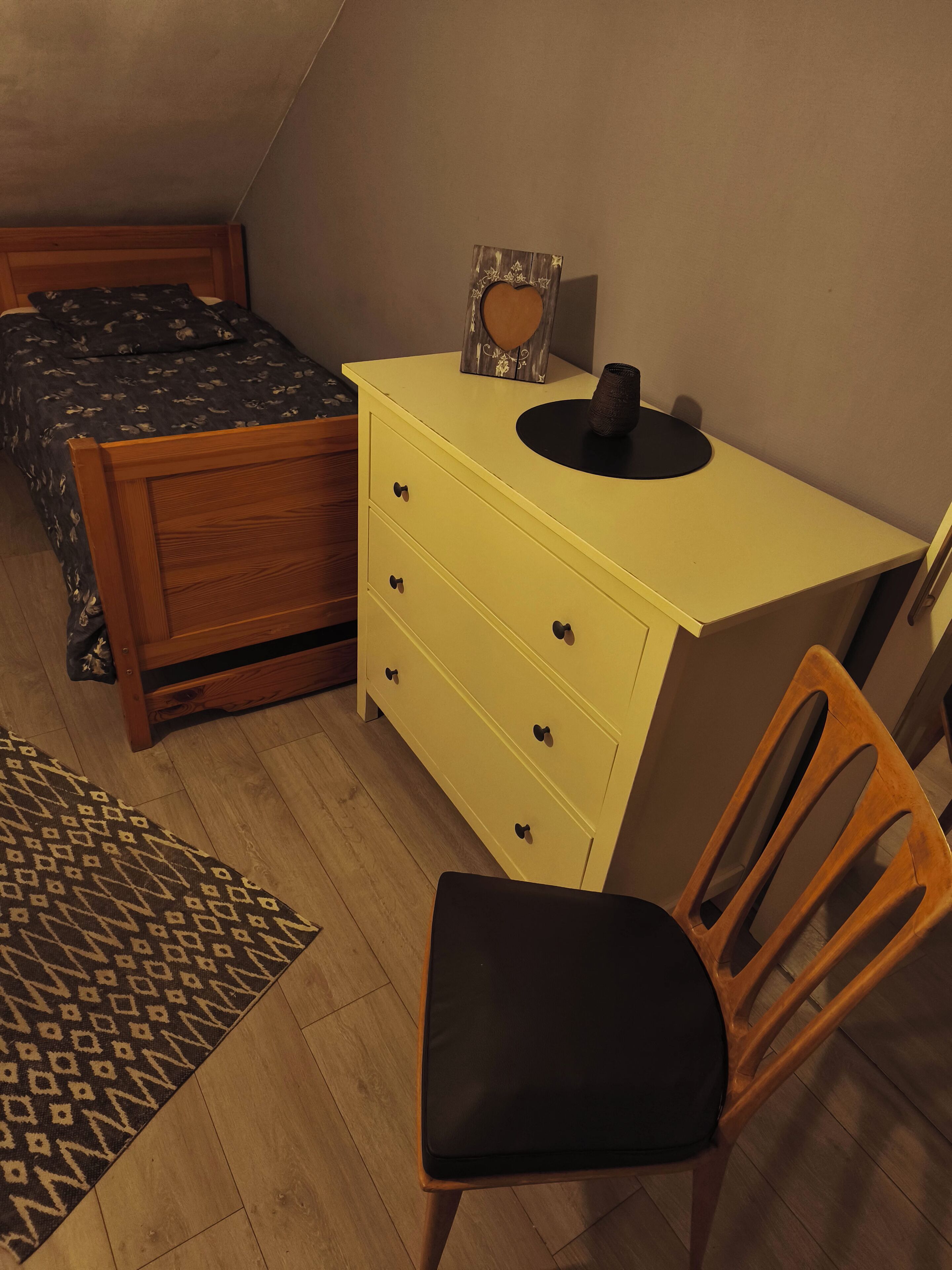 Une chambre à coucher avec un lit, une commode jaune, une chaise et un tapis à motifs.