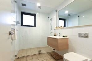 A modern bathroom with a glass shower enclosure, a wooden vanity, and a large mirror. - 2-bedroom Apartment in the Heart of Batemans Bay (Batemans Bay)