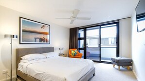 Ein modernes Hotelzimmer mit einem großen Bett, einem Deckenventilator, einem Fenster mit Blick, einem Sessel und einem kleinen Tisch.