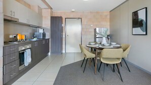 Une cuisine moderne avec des meubles gris, un four encastré et un coin repas comprenant une table et des chaises.