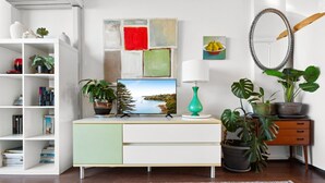 Un saló modern amb un moble blanc i verd, un televisor de pantalla plana, un vas verd i diverses plantes en testos.