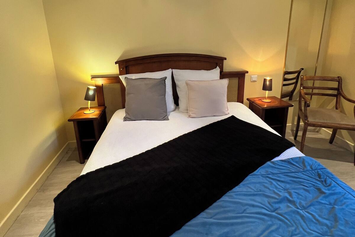 A hotel room with a bed, two bedside tables, a chair, and a mirror on the wall.