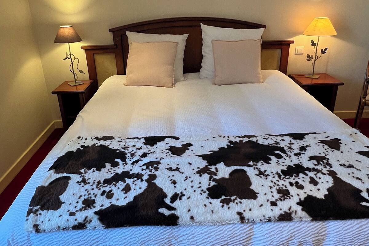 A bed with a white and brown patterned blanket, two white pillows, and a wooden headboard. There are two bedside tables with lamps on either side of the bed.