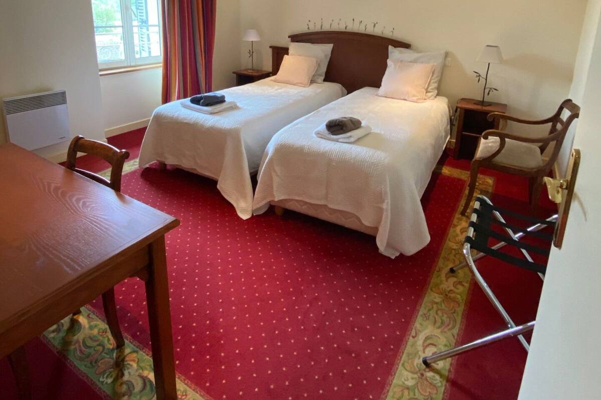 A hotel room with two beds, a dining table, and a window with curtains.