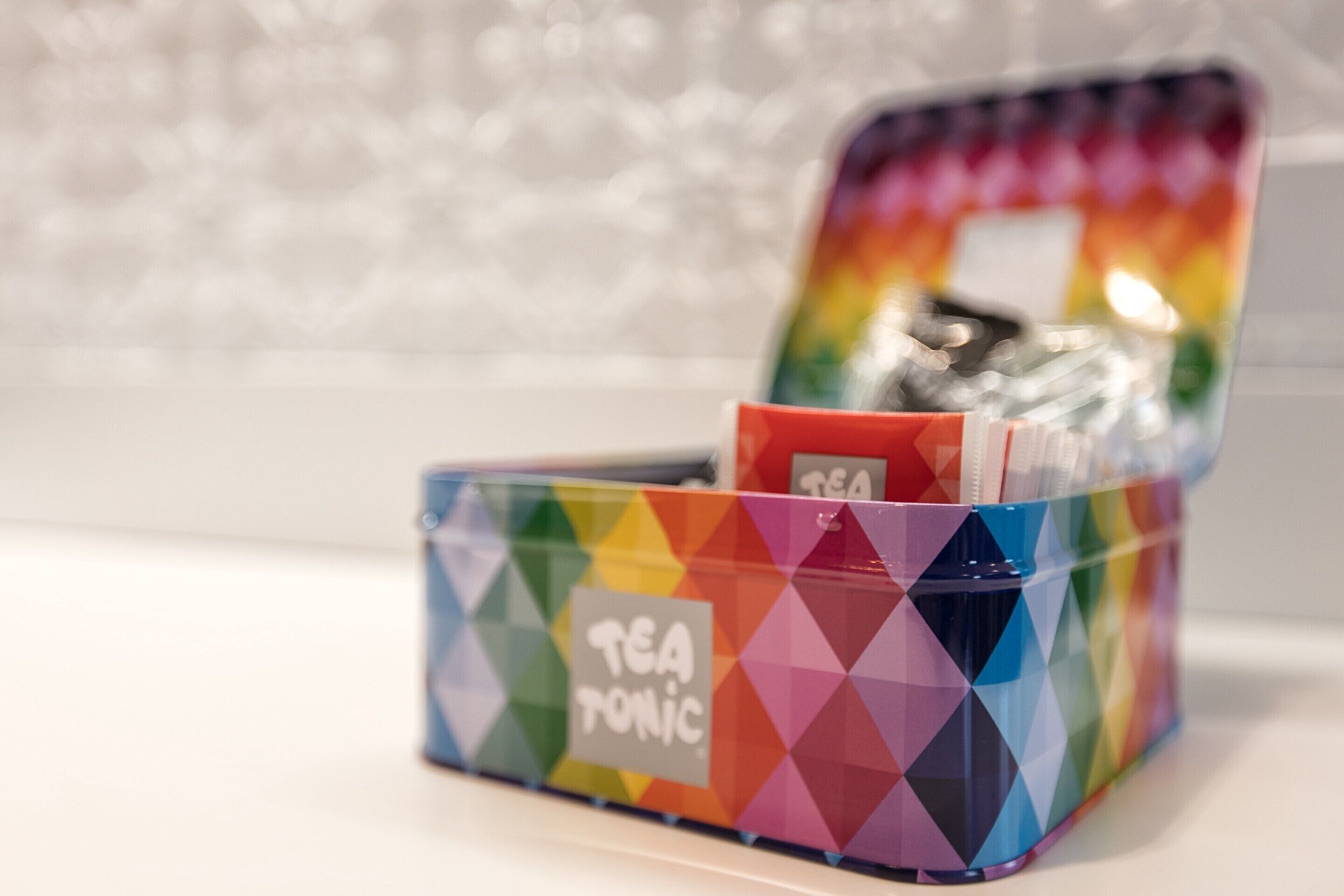 Una lata de té con un estampado geométrico colorido y la etiqueta "TEA TONIC" sobre una superficie blanca.