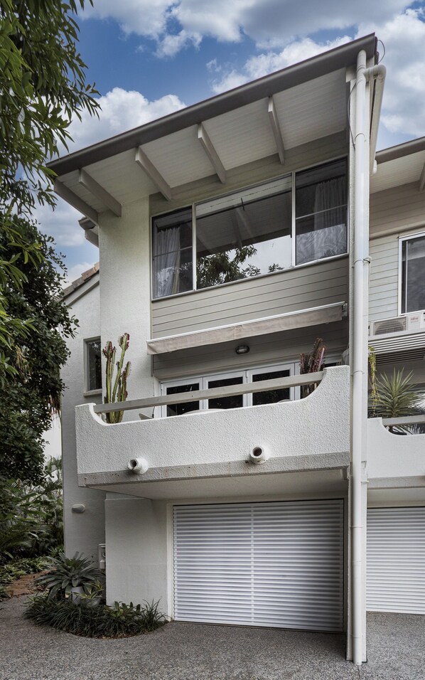 Um edifício de dois andares com varanda, garagem e janela com cortina.