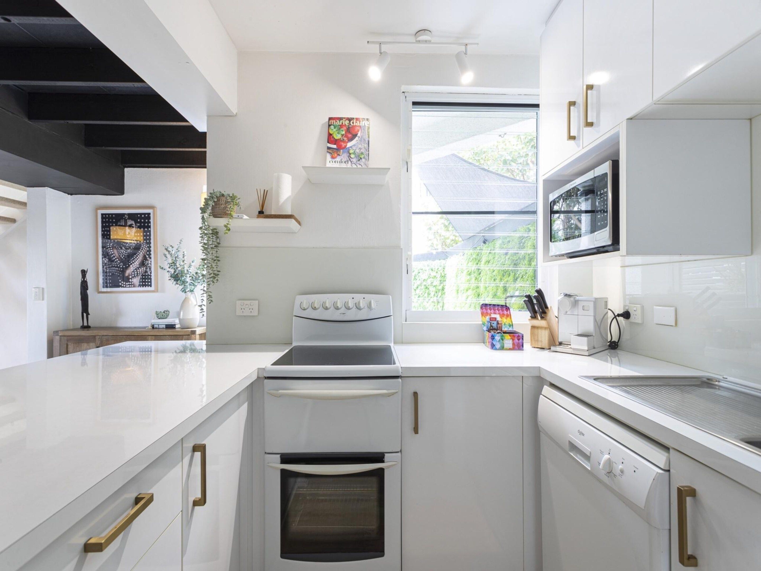 Una cocina moderna con armarios blancos, horno empotrado, microondas y una ventana que proporciona luz natural.