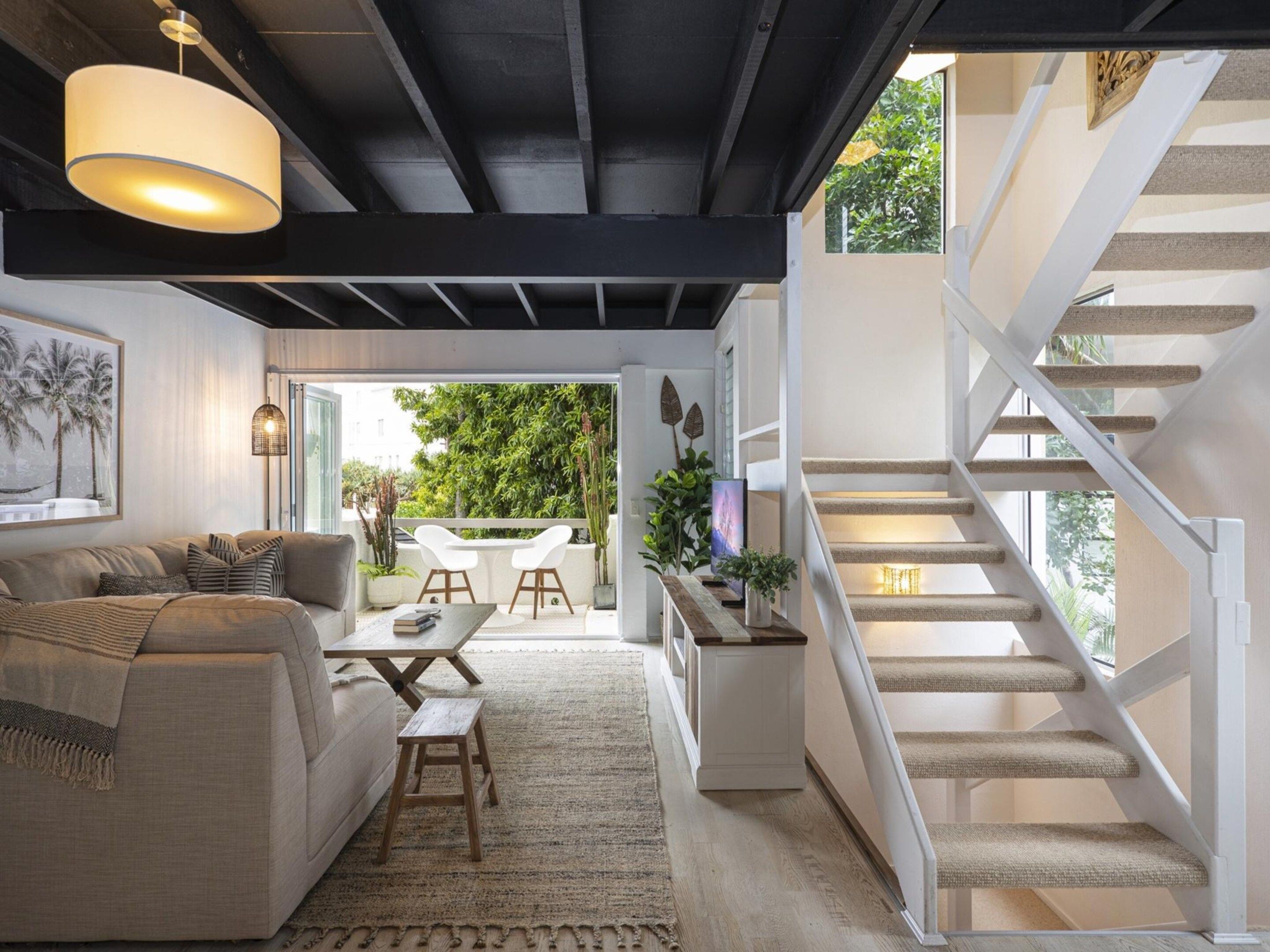 Un intérieur moderne avec un escalier, un canapé, une table à manger et une vue sur l’extérieur.