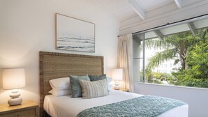 Ein Schlafzimmer mit einem großen Bett, zwei Nachttischen mit Lampen, einem gewebten Kopfteil, Blick ins Grüne durch ein Fenster und einem gerahmten Bild an der Wand.