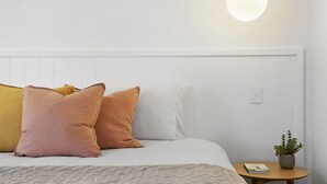 A neatly made bed with white and peach pillows, a round pendant light, and a small table with a plant and book. - Spacious 4-bed Villa With Mediterranean Charm (Gold Coast)