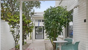 A courtyard with a white brick wall, a metal gate, and a small garden area with green chairs and a table. - Spacious 4-bed Villa With Mediterranean Charm (Gold Coast)