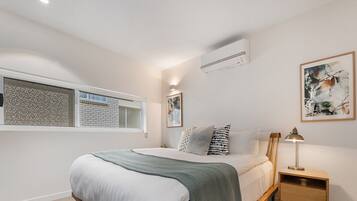 A bedroom with a bed, a nightstand, a lamp, a window, and an air conditioning unit.