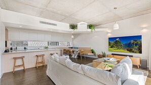 Een moderne keuken met een centraal eiland, houten krukken en een eethoek met tafel en stoelen.
