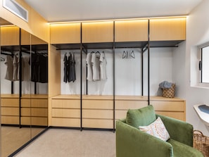 A modern walk-in closet with wooden shelving, a mirrored section, and a green armchair. - Luxury 5-floor Unit With Ocean Views Near Beach (Sunshine Coast)