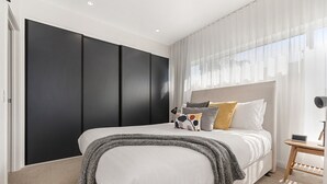 Een slaapkamer met een groot bed, een zwarte garderobe, een nachtkastje met een lamp en dunne gordijnen.
