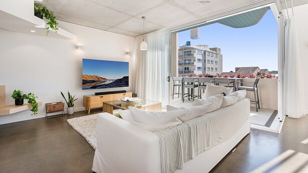 Een moderne woonkamer met een witte bank, een flatscreentelevisie en een eethoek met een tafel en stoelen.