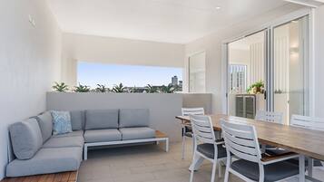A modern outdoor living space with a sofa, dining table, chairs, and a view of the city skyline.