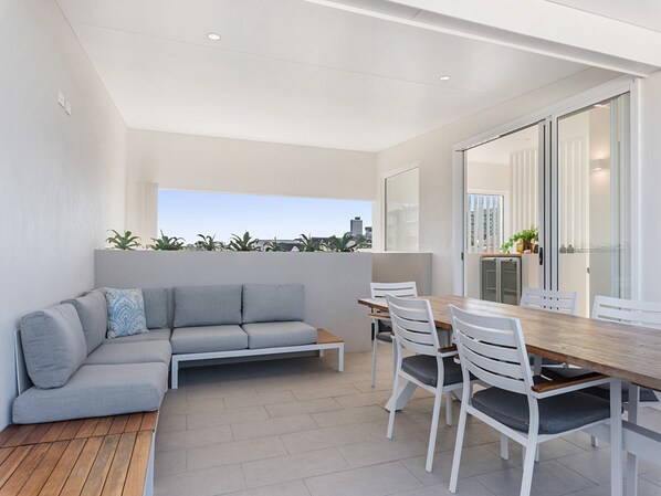A modern outdoor living space with a sofa, dining table, chairs, and a view of the city skyline. - Luxury 5-floor Unit With Ocean Views Near Beach (Sunshine Coast)