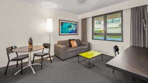 Habitación de hotel con sofá, dos sillones, una mesita, lámpara y ventana con cortinas.