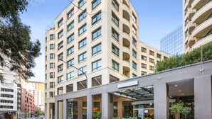 Un hotel moderno con fachada curva, ventanas amplias y una zona de entrada cubierta con plantas en macetas.