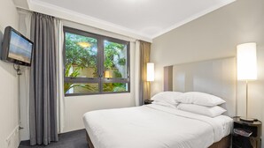 Una habitación de hotel con cama, televisión, ventana con cortinas y lámpara de noche.