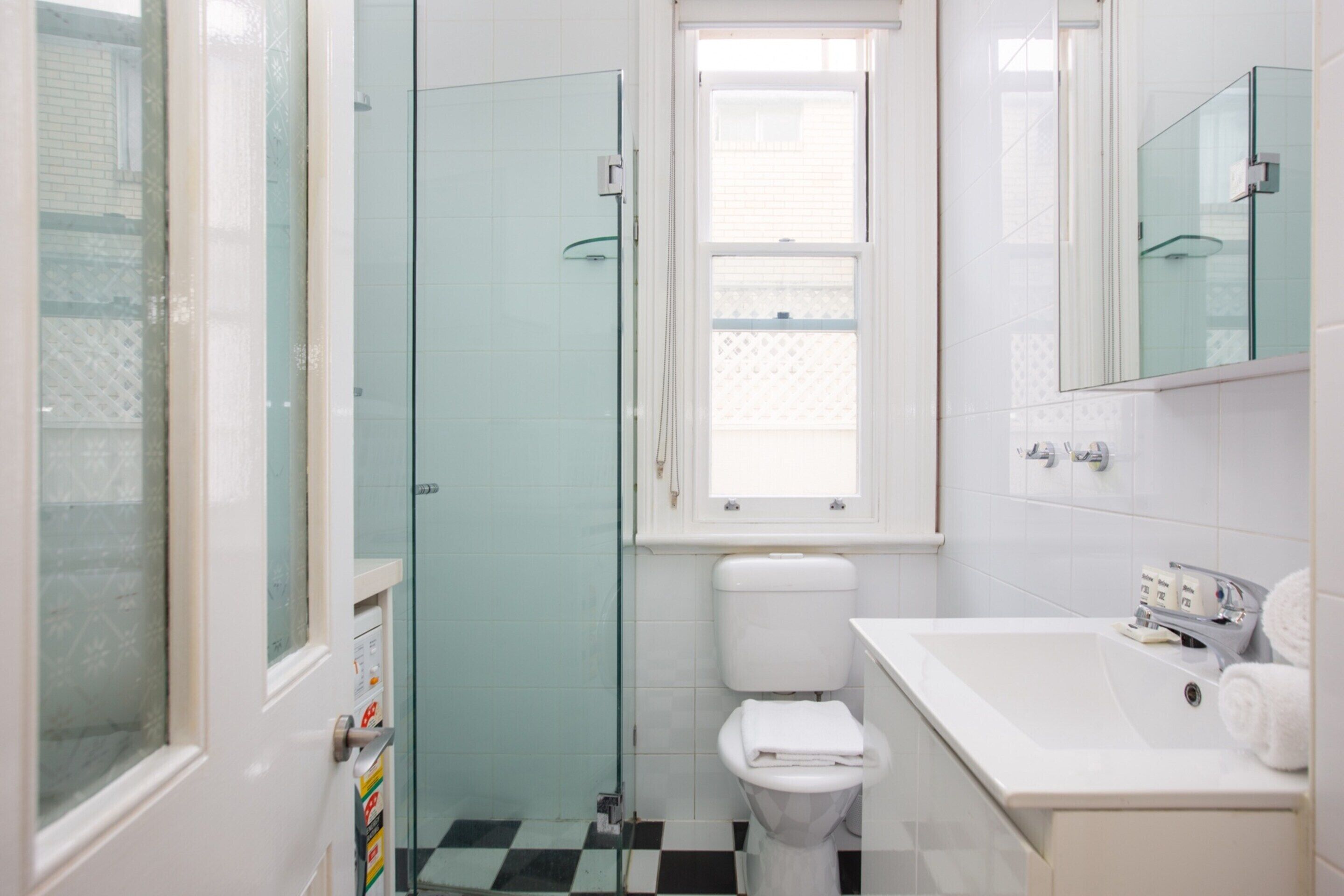 A bathroom with a glass shower enclosure, a toilet, a sink with a mirror, and a window.