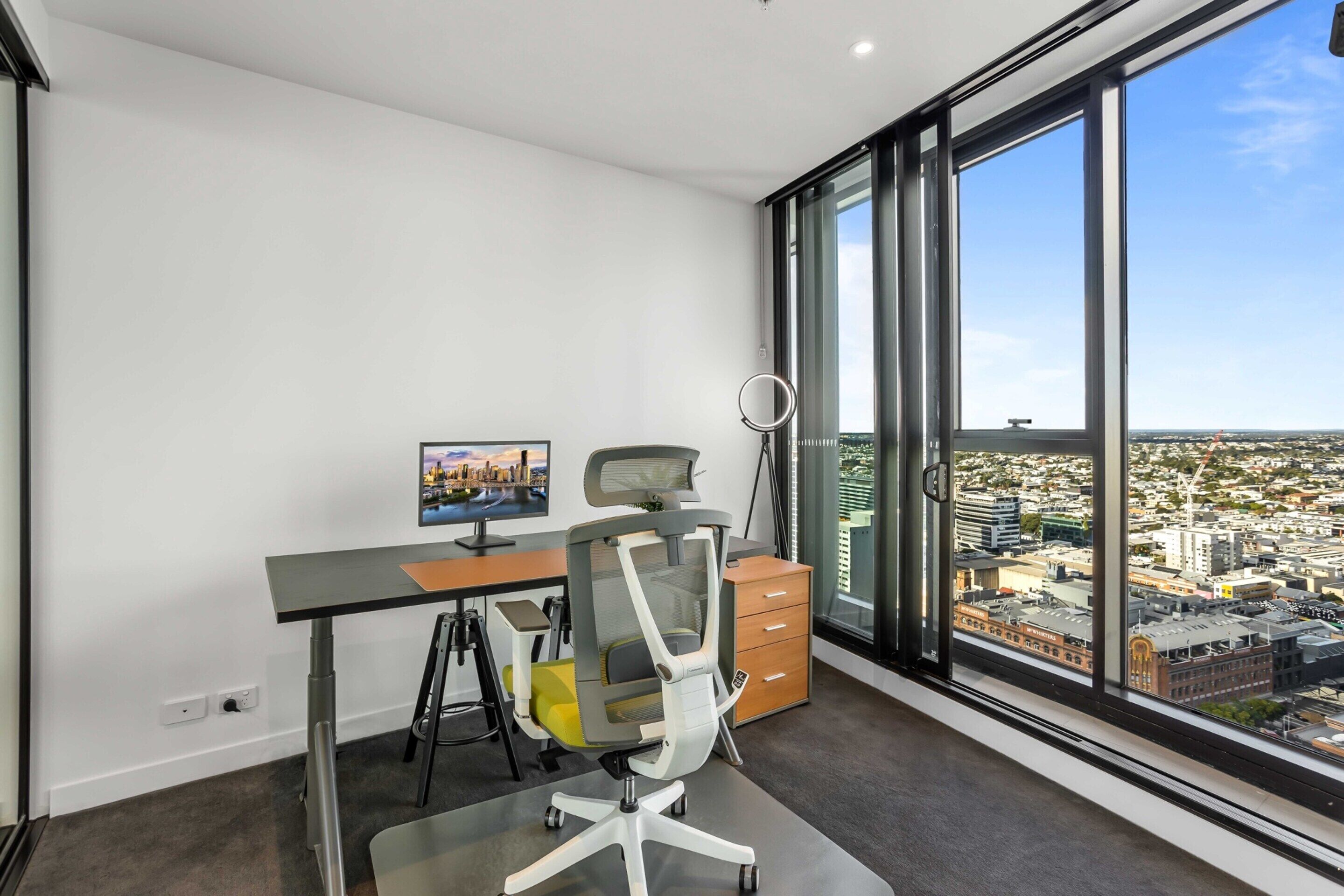 Un espacio de oficina moderno con un escritorio, una silla de oficina y un ventanal con vistas a la ciudad.