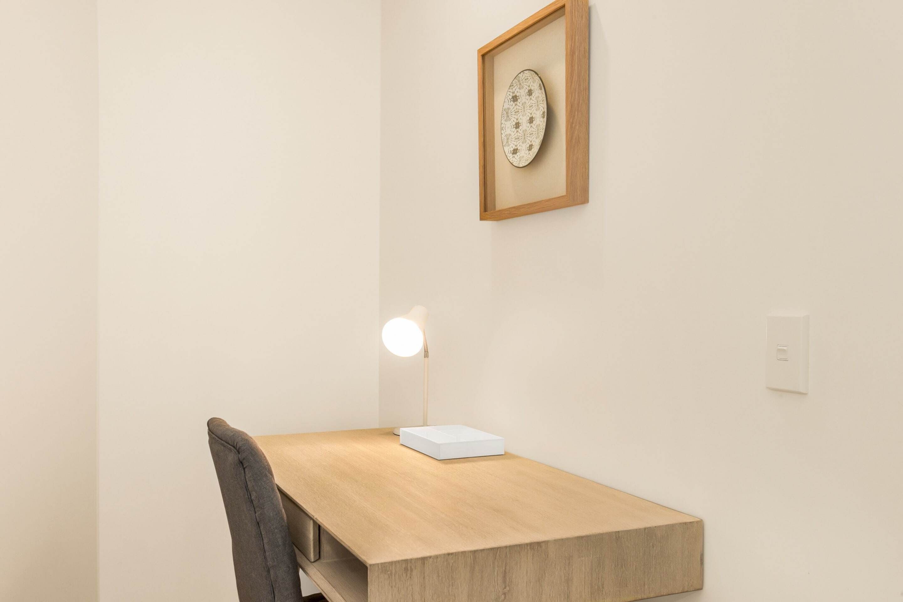A minimalist workspace with a wooden desk, a white lamp, and a framed picture on the wall.