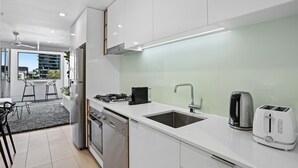 A modern kitchen with white cabinets, a stainless steel dishwasher, a gas stove, a sink, a kettle, and a toaster. - Stellar Location With Parking, Pool & Gym Access (Brisbane)