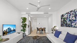 A modern living room with a white sofa, a coffee table, a TV, and a large abstract painting. - Stellar Location With Parking, Pool & Gym Access (Brisbane)