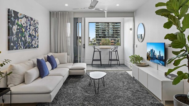 A modern living room with a sofa, a small table, a TV, and a balcony with a city view. - Stellar Location With Parking, Pool & Gym Access (Brisbane)