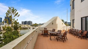 Una terrazza sul tetto con vista su un fiume e un ponte, arredata con tavoli e sedie.